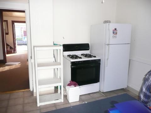 A small kitchen with a white fridge, gas stove, and empty shelves.